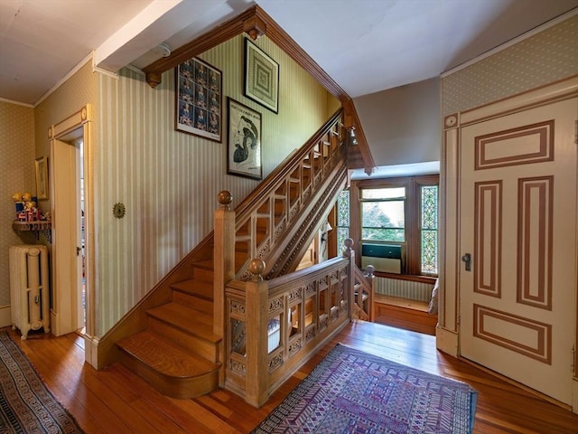stairs featuring radiator, wood-type flooring, wallpapered walls, and ornamental molding