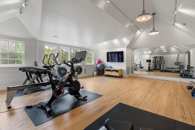 workout room featuring track lighting, lofted ceiling, and light wood-type flooring