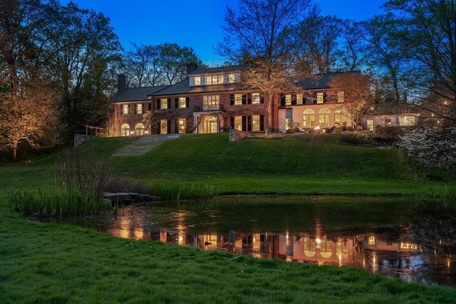 back house at dusk with a yard and a water view