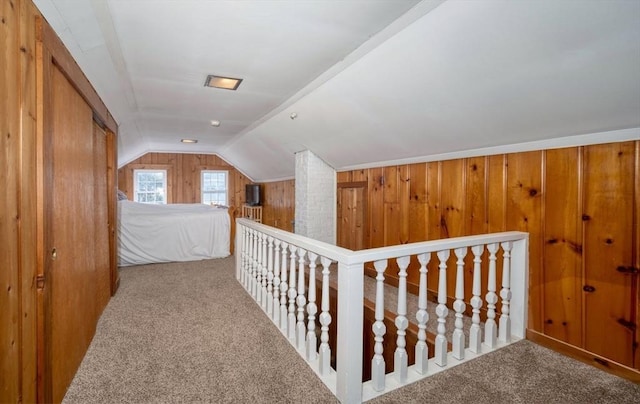 corridor with vaulted ceiling, wood walls, and carpet flooring