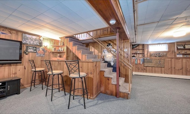 bar with a dry bar, carpet, wooden walls, and stairway