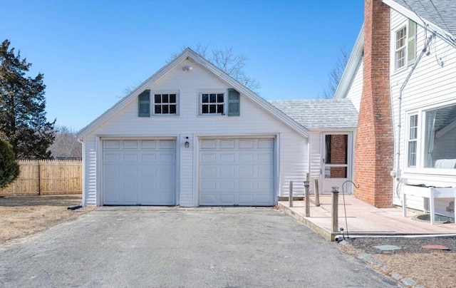 exterior space with a garage, roof with shingles, a chimney, and fence