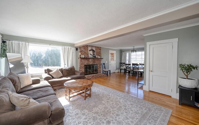 living area featuring a notable chandelier, a brick fireplace, light wood-type flooring, and crown molding