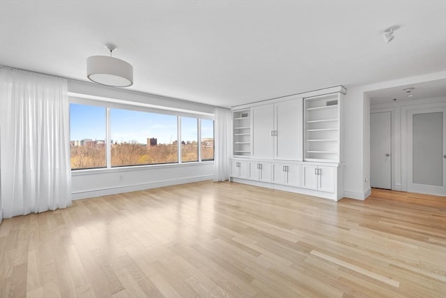 unfurnished living room with light wood-type flooring, baseboards, and built in features