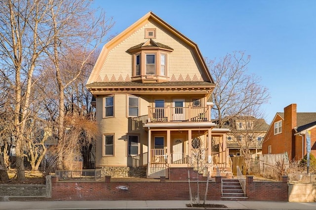 dutch colonial featuring a porch, a fenced front yard, a balcony, and a gambrel roof