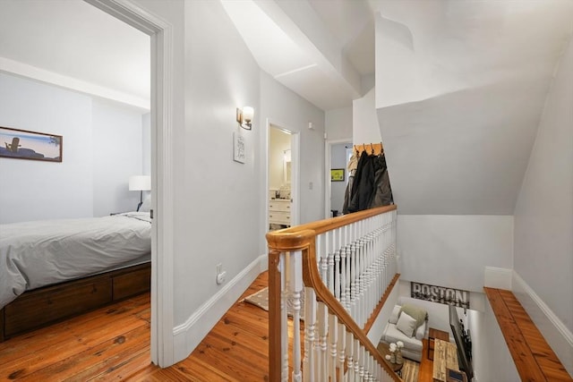 corridor with baseboards, hardwood / wood-style floors, and an upstairs landing