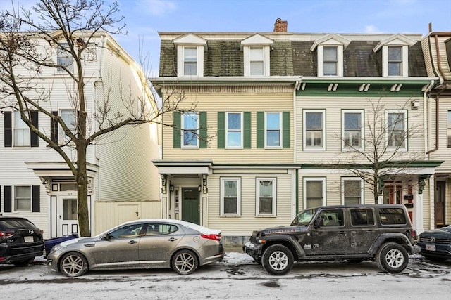view of front of house featuring mansard roof and a chimney