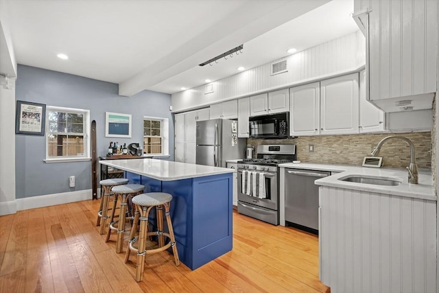 kitchen featuring visible vents, a kitchen breakfast bar, a sink, light wood finished floors, and stainless steel appliances