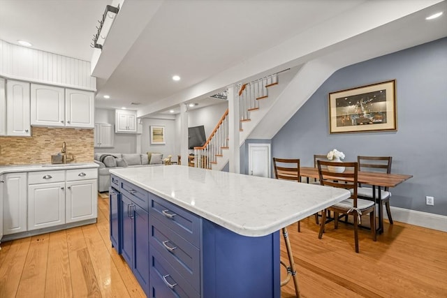 kitchen with a sink, light wood-style floors, white cabinetry, a kitchen bar, and backsplash