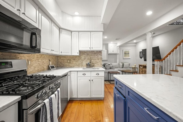 kitchen with appliances with stainless steel finishes, a sink, white cabinetry, light wood-type flooring, and blue cabinets