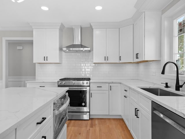 kitchen featuring sink, wall chimney range hood, appliances with stainless steel finishes, and white cabinets