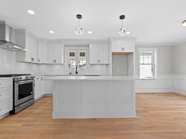 kitchen with white cabinets, wall chimney exhaust hood, a wealth of natural light, and stainless steel stove