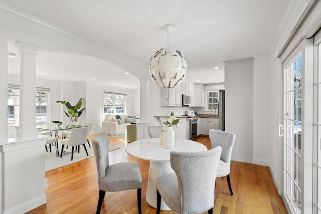 dining area featuring light hardwood / wood-style floors, an inviting chandelier, crown molding, and decorative columns