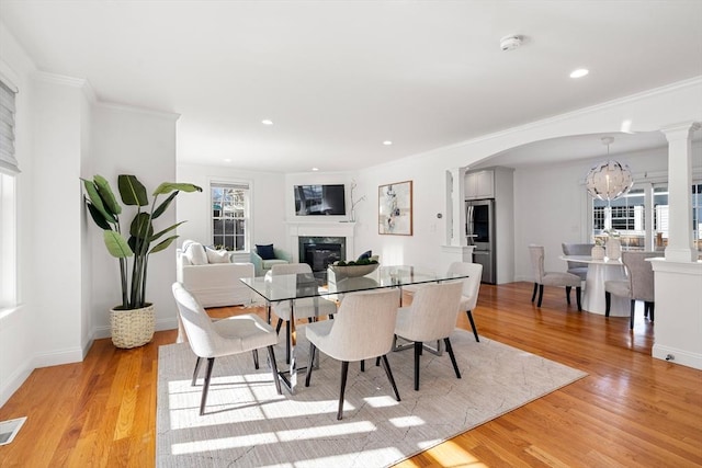 dining room with light hardwood / wood-style flooring, an inviting chandelier, a high end fireplace, and decorative columns