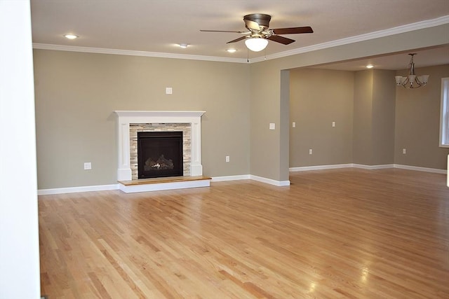 unfurnished living room with ornamental molding, a stone fireplace, ceiling fan with notable chandelier, and light wood-type flooring