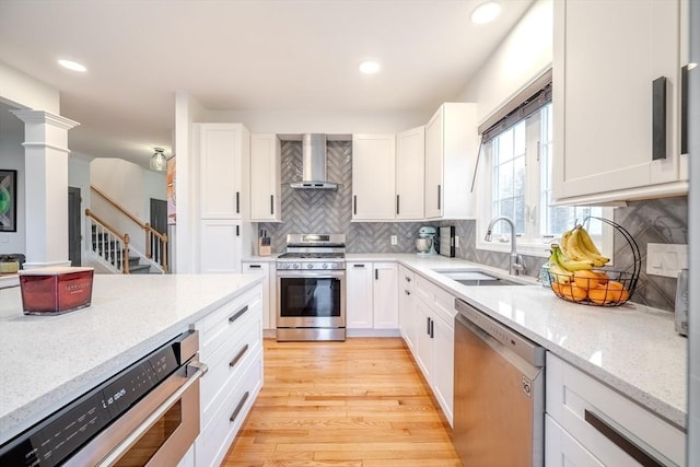 kitchen with appliances with stainless steel finishes, tasteful backsplash, a sink, white cabinets, and wall chimney exhaust hood
