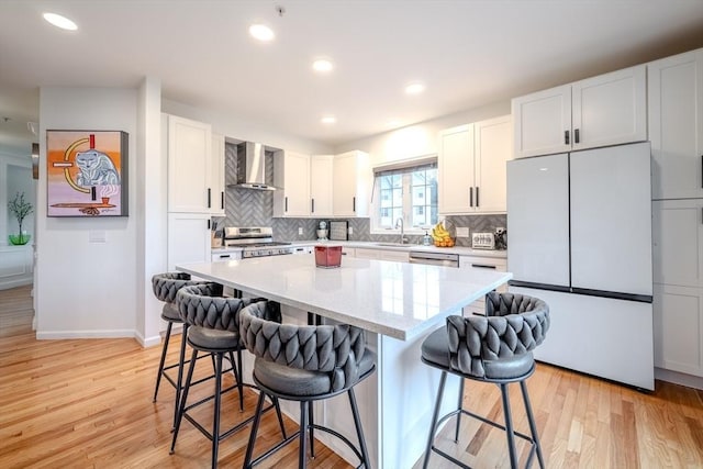 kitchen with wall chimney range hood, light wood-type flooring, tasteful backsplash, a sink, and appliances with stainless steel finishes