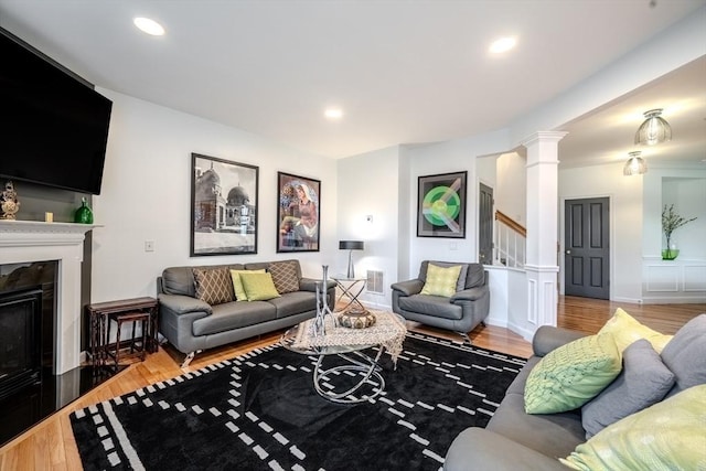 living room featuring visible vents, decorative columns, wood finished floors, stairway, and a fireplace with flush hearth