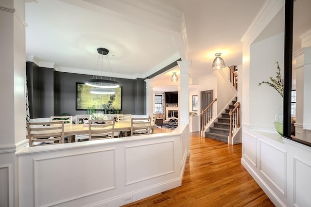 interior space with crown molding, a decorative wall, light wood-style flooring, ornate columns, and stairway