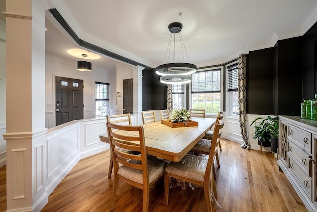 dining area featuring ornamental molding, light wood-style flooring, and a decorative wall
