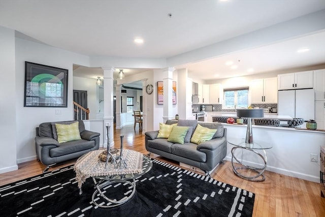 living area featuring baseboards, light wood finished floors, ornate columns, and stairs