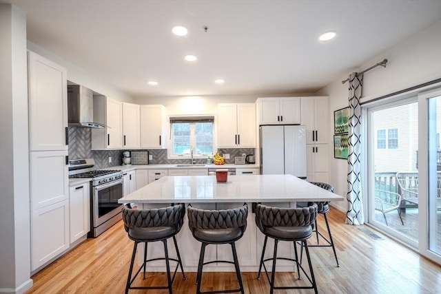 kitchen with a sink, stainless steel gas stove, a kitchen breakfast bar, wall chimney exhaust hood, and freestanding refrigerator