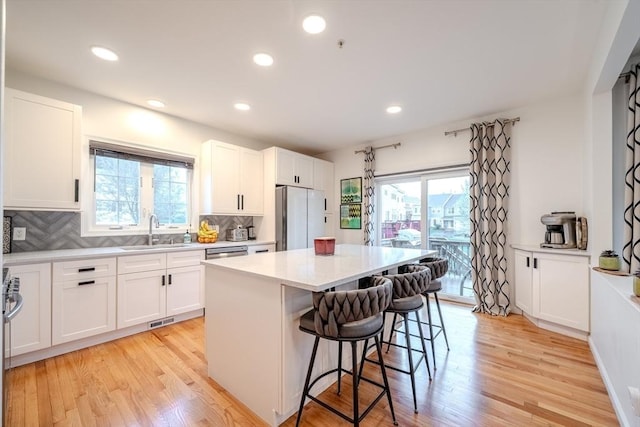 kitchen with a kitchen island, a kitchen bar, a sink, freestanding refrigerator, and light wood-style flooring