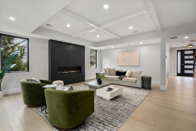 living room with beam ceiling, a fireplace, coffered ceiling, and light wood-type flooring