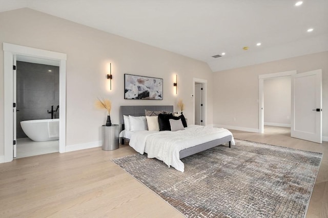 bedroom with ensuite bathroom, light hardwood / wood-style floors, and lofted ceiling