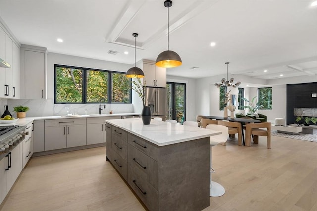 kitchen with high end refrigerator, a kitchen island, decorative light fixtures, light hardwood / wood-style floors, and light stone counters