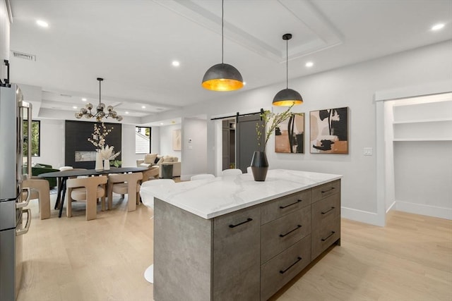 kitchen featuring a center island, decorative light fixtures, a barn door, and light stone counters