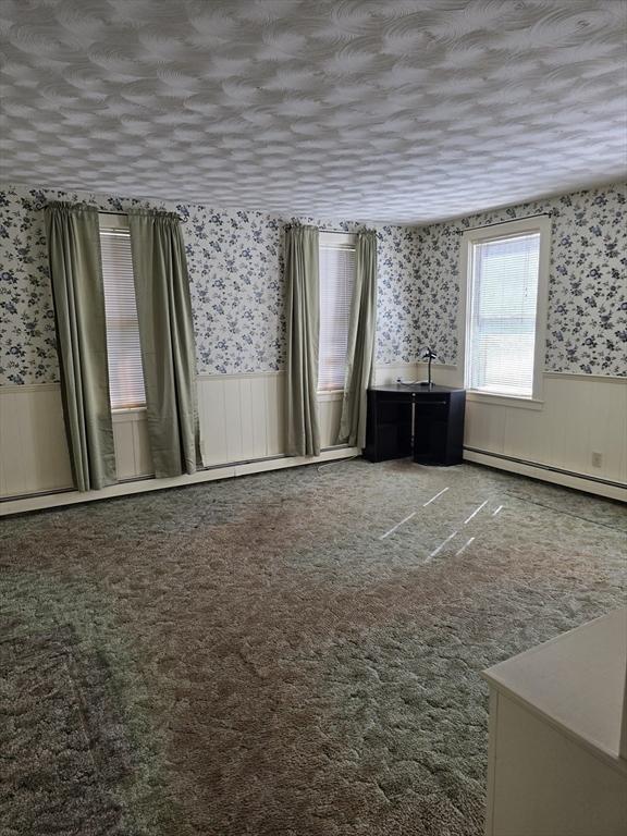 interior space featuring wallpapered walls, carpet flooring, a wainscoted wall, and a baseboard heating unit