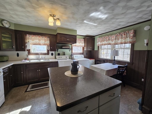 kitchen featuring a sink, a center island, wood walls, wainscoting, and washing machine and clothes dryer