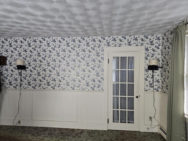 unfurnished room featuring wallpapered walls, a wainscoted wall, a baseboard heating unit, and carpet floors