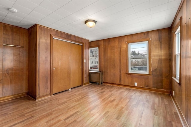 unfurnished bedroom featuring light wood finished floors, wooden walls, baseboards, and a closet