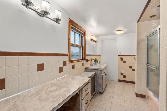 full bathroom with tile walls, wainscoting, combined bath / shower with glass door, vanity, and tile patterned flooring