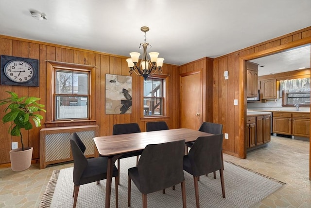 dining room with a chandelier, stone finish floor, wood walls, and radiator heating unit