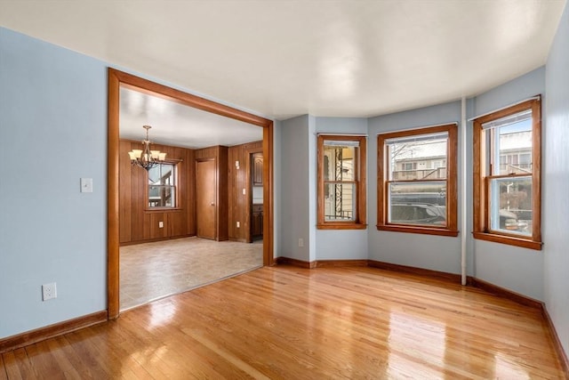 empty room with a healthy amount of sunlight, light wood-style flooring, a chandelier, and baseboards