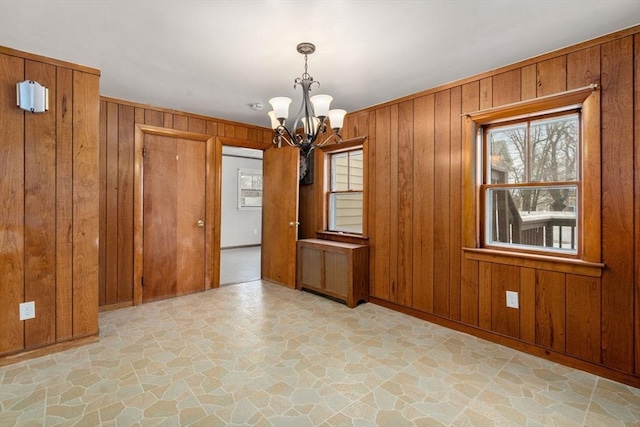 unfurnished room with a notable chandelier, wooden walls, radiator heating unit, and stone flooring