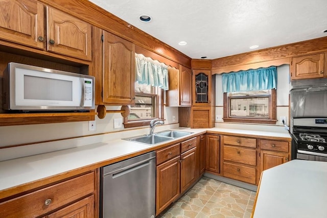 kitchen featuring stainless steel appliances, light countertops, brown cabinetry, stone finish flooring, and a sink