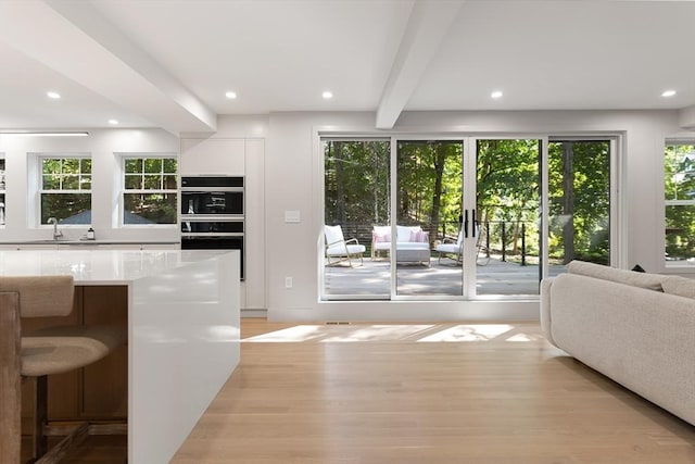 interior space featuring french doors, beam ceiling, light hardwood / wood-style floors, white cabinetry, and a breakfast bar area