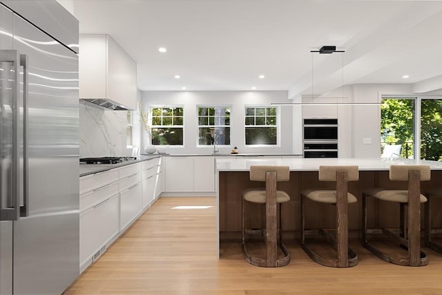 kitchen with decorative backsplash, appliances with stainless steel finishes, a kitchen breakfast bar, decorative light fixtures, and white cabinets