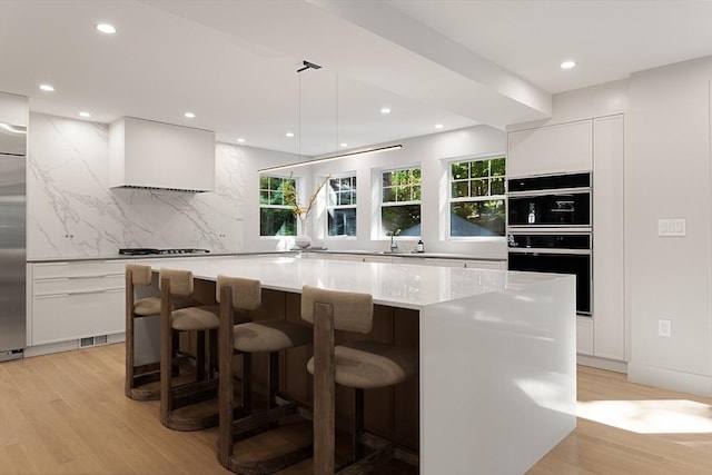 kitchen with a center island, white cabinets, decorative backsplash, light wood-type flooring, and decorative light fixtures