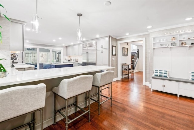 kitchen with white cabinetry, hanging light fixtures, dark wood-type flooring, a kitchen bar, and stainless steel built in fridge