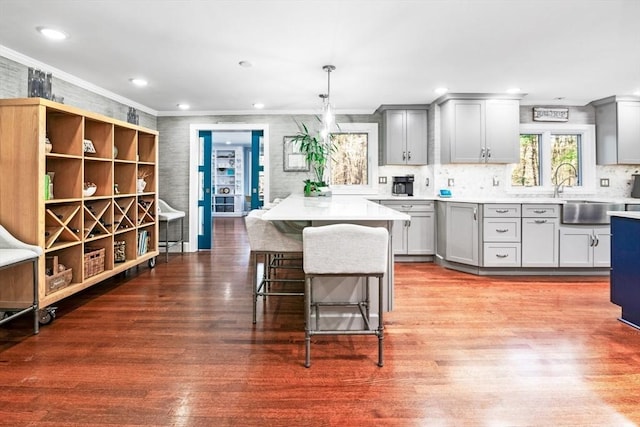 kitchen with gray cabinetry, sink, decorative light fixtures, wood-type flooring, and a breakfast bar area