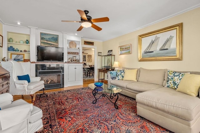 living room featuring crown molding, built in features, light hardwood / wood-style floors, and ceiling fan