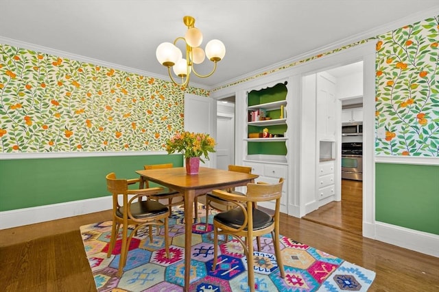 dining space featuring wallpapered walls, ornamental molding, a chandelier, baseboards, and wood finished floors