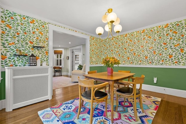 dining space featuring wallpapered walls, a chandelier, crown molding, wood finished floors, and baseboards