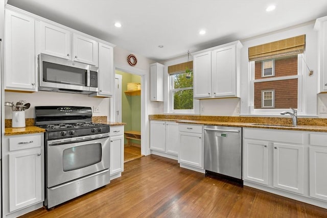 kitchen with stainless steel appliances, a sink, white cabinetry, dark wood finished floors, and light stone countertops