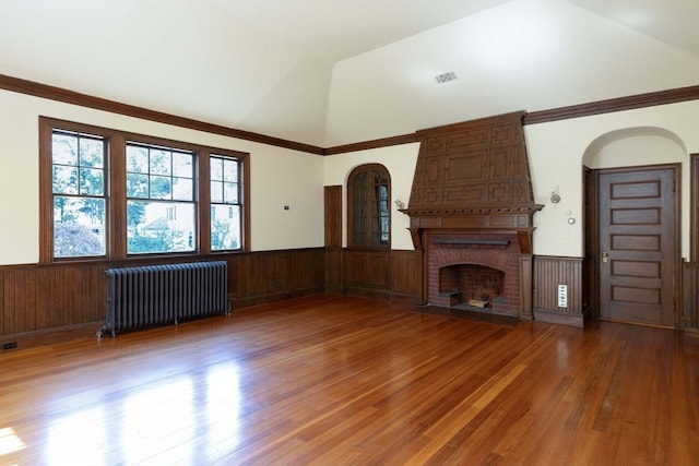 unfurnished living room with hardwood / wood-style floors, radiator, vaulted ceiling, wood walls, and a fireplace